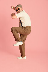 Fototapeta premium Portrait of senior man in stylish classical clothes posing, serving baseball ball over pink background. Sport club