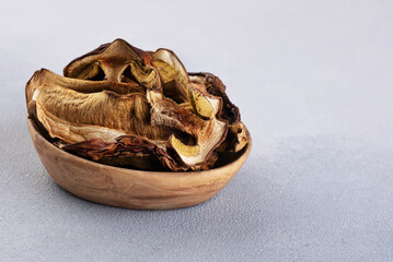 Dried Boletus edulis (king bolete) in a wooden bowl on a light background.