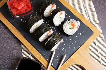Sushi of rice, cucumber fish and cheese on a serving board with chopsticks. Top view