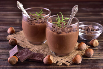 Mousse with dark chocolate with hazelnuts in glasses on a dark wooden background.	