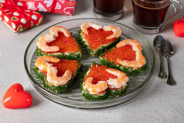 Canape form of hearts with red caviar and shrimp on white plate on gray background, Valentine's Day breakfast idea