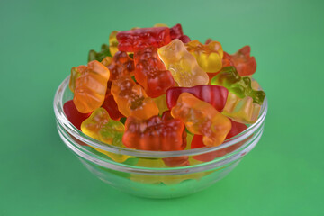 Many multi-colored jelly bears in a plate on a green background. Close-up.
