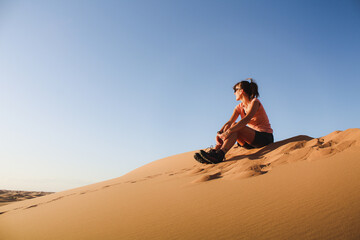 Sitting on a desert dune, the girl watching left