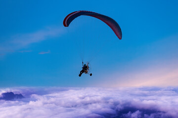 Silhouette of the paraglider  with paramotor transportation control flying through soft sunlight  fog white cloud blue sky.