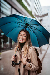 A beautiful smiling young woman walking through the city with an umbrella.