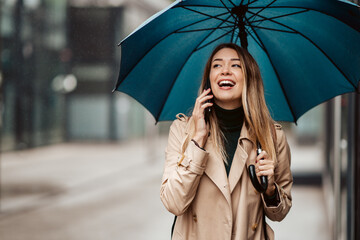 A beautiful young woman standing under an umbrella and talking on the phone.
