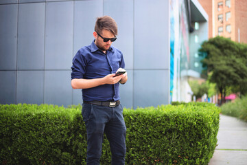 Young entrepreneur using mobile phone at office outdoors. Young business man using mobile phone.