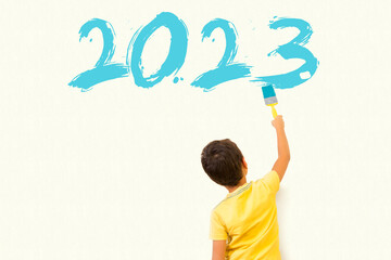 Cute little boy ( kid ) drawing new year 2023 with painting brush on wall background