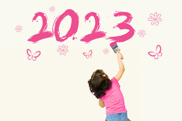 Cute little girl writing new year 2023 using painting brush on wall background