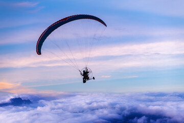 Silhouette of the paraglider  with paramotor transportation control flying through soft sunlight ...