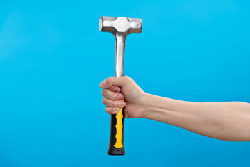 Human hand holding hammer on blue background