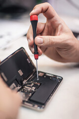 Workplace top view, close-up. Repairman disassembles smartphone with screwdriver in an electronics...