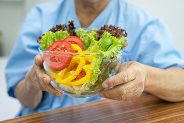 Asian senior or elderly old lady woman patient eating breakfast vegetable healthy food with hope and happy while sitting and hungry on bed in hospital.