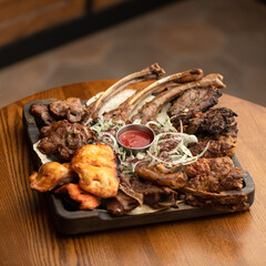 Fried lamb ribs on square wooden plate with red sauce and pickled onions. Dish on wooden table. Serving dish. Restaurant photo menu. Soft focus, top view. 