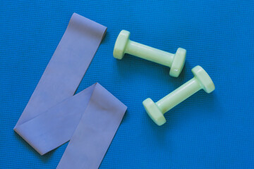 Top view of dumbbells and fitness ribbon on blue sports mat. Flat lay, copy space. Home training...