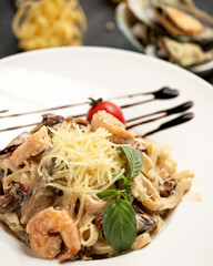 Italian pasta withseafood, parmesan cheese, basil and tomato. Traditional italian spaghetti on plate. Mediterranean menu. Blurred dark background. Vegetarian dish. Copy space. Top view