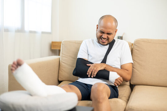 Man suffered pain from accident fracture broken bone injury with leg splints in cast neck splints collar arm splints sling support arm in living room. Social security and health insurance concept.