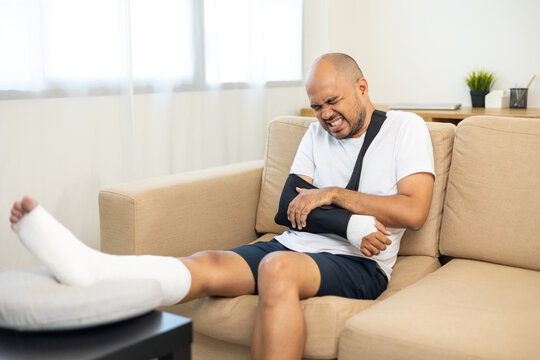 Man suffered pain from accident fracture broken bone injury with leg splints in cast neck splints collar arm splints sling support arm in living room. Social security and health insurance concept.