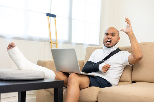 Recovery man stressed from accident fracture broken bone injury with leg splints in cast neck splints collar sling support arm work with laptop. Social security and health insurance concept.