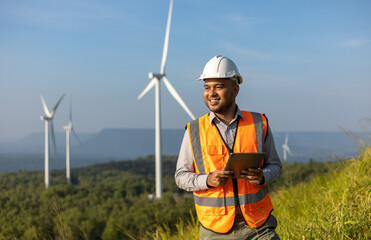 Engineer India man working with tablet at windmill farm Generating electricity clean energy. Wind turbine farm generator by alternative green energy. Asian engineer checking control electric power