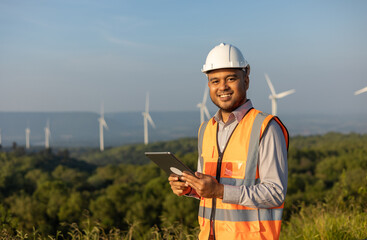 Fototapeta premium Engineer India man working with tablet at windmill farm Generating electricity clean energy. Wind turbine farm generator by alternative green energy. Asian engineer checking control electric power