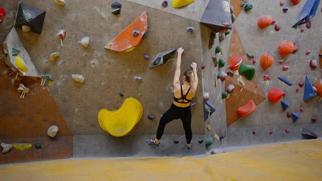 Woman climbs up grabbing and stepping on formed holds