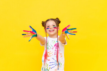 A teenage girl, smeared with multicolored paint, shows her palms and smiles broadly. The art of drawing for schoolchildren. Courses in freehand drawing. Colors of life.