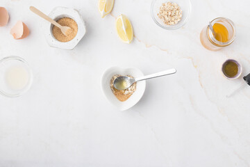 Flatlay with homemade beauty products: fresh ingredients like oat, honey, lemon, banana, egg, olive oil. Female hand holding a jar of cream. Overhead view, copy space.