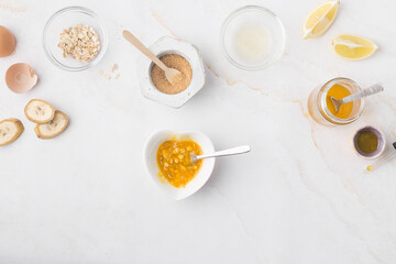 Flatlay with homemade beauty products: fresh ingredients like oat, honey, lemon, banana, egg, olive oil. Female hand holding a jar of cream. Overhead view, copy space.