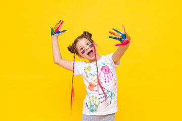 The child is playing with colorful paints. A little girl stained with paint for drawing on a yellow isolated background. Art courses for schoolchildren. Creative education of children.