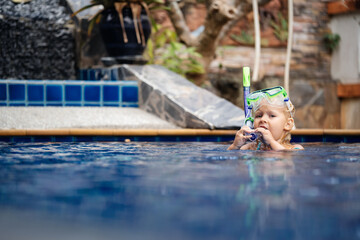 A child in the pool puts on a mask and snorkel for diving.