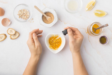 Flatlay with homemade beauty products: fresh ingredients like oat, honey, lemon, banana, egg, olive oil. Female hand holding a jar of cream. Overhead view, copy space.