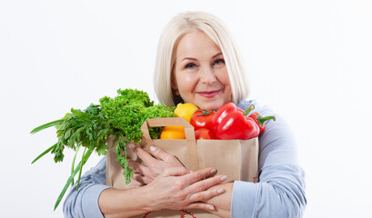 Happy woman with blond hair and beautiful smile holds a bag of vegetables and herbs red pepper and green lettuce in her hands for a healthy diet with vitaminswith. Concept healthy food vegetable