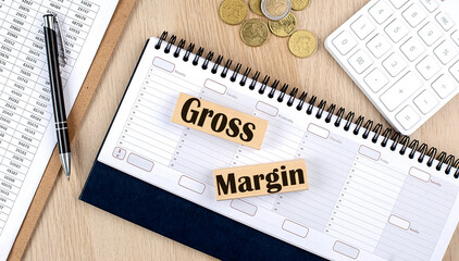 GROSS MARGIN word written on wooden block on planner with coins, clipboard and a calculator