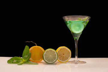 Verre à cocktail de couleur vert avec des fruits sur fond noir.	