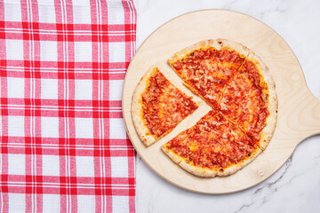 pizza on wooden cutting board with red and white checkered cloth on marble background