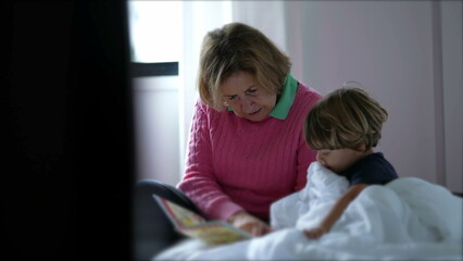 Grandmother reading a book to grandchild. Candid grandparent tells a bedtime story to toddler boy child