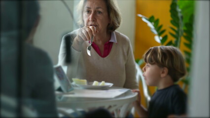 Grandmother feeding grandson at lunch time in terrace while in conversation. Candid grandma feeds small boy fruit