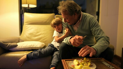 Grandfather and grandson hanging out together in living room couch. Authentic real life family generational relationship at night sitting on couch