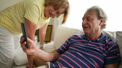 Mature older couple speaking with family member holding smartphone device. Senior married couple waving hello using cellphone sitting on couch at living room