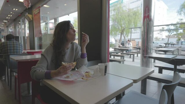 Mujer comiendo hamburguesa en restaurante comida r&aacute;pida (Formato LOG para edici&oacute;n y correcci&oacute;n de color profesional)