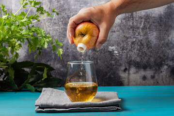 Hand holding a fruit, apple, which has a spout through which it pours the juice into the glass as...