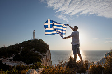 man with greece flag looking at sunset above the sea