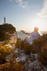 man with drone at the cliff near sea sunset above the lighthouse
