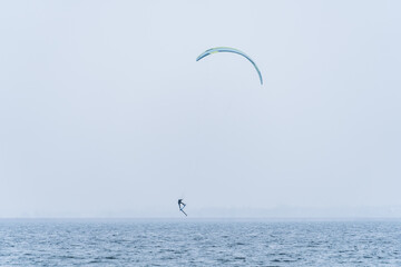 Hydrofoil Kitesurfer jumping in misty and cold winter conditions