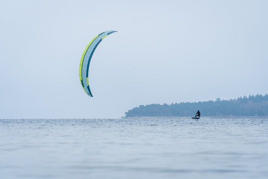 Wide shot of Hydrofoil Kitesurfer in winter conditions at the baltic sea with forest in the background