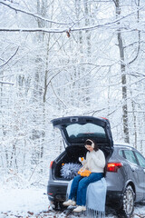 In the middle of a winter forest, a young woman in a car with a Christmas tree