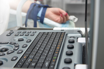 Close up of the keyboard of a medical device for ultrasound during surgery against the background of the patient's hand. During the surgical operation, the patient undergoes an ultrasound examination