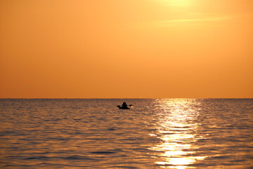 Dark figure of sportsman rowing alone on his kayak boat on sea water at sunset. Active extreme sports concept