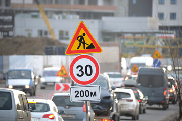 Roadworks warning traffic signs of construction work on city street and slowly moving cars